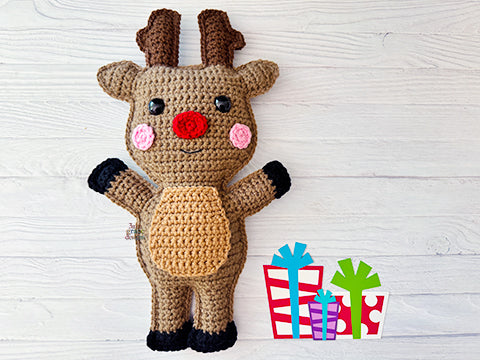 Kawaii amigurumi ragdoll style crochet pattern for a reindeer toy with antlers, red nose, and pink cheeks on a light wooden background with colorful gift boxes.
