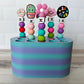 Colorful beaded crochet hooks in a crochet hook holder on a wooden surface with a white tiled wall background