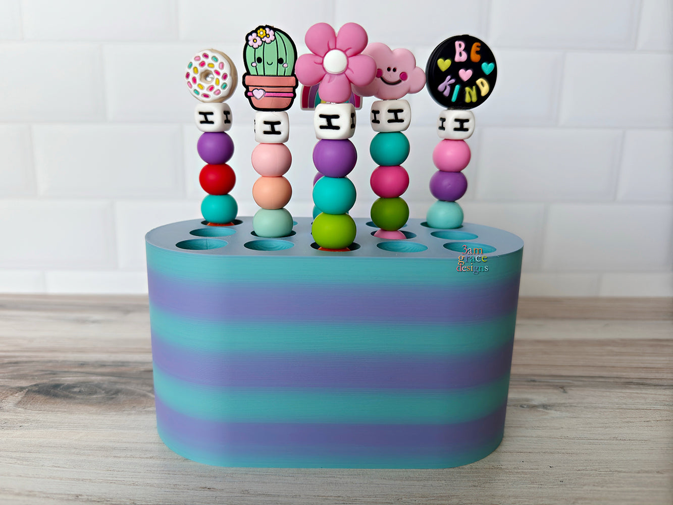 Colorful beaded crochet hooks in a crochet hook holder on a wooden surface with a white tiled wall background