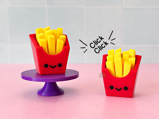 Two red fidget clickers with yellow french fries on a pink surface with a white tiled background.