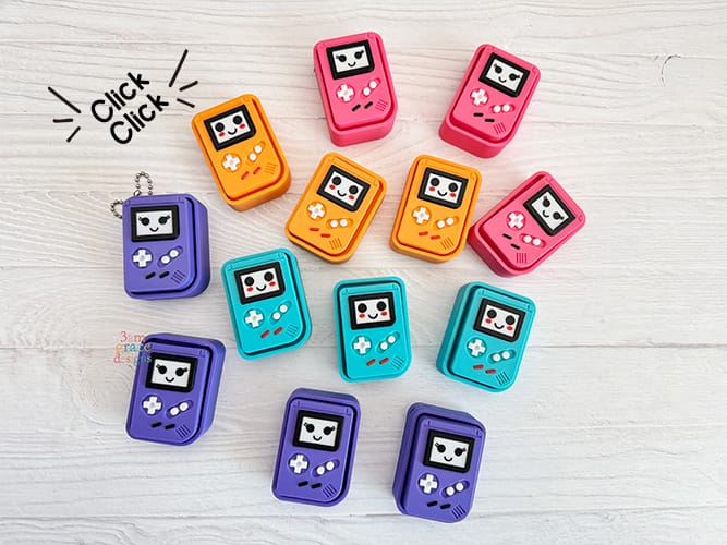 Colorful Game Boy keychain clickers on a light wooden surface with 'Click Click' text.