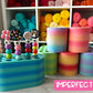 Colorful crochet hook holders on a wooden surface with yarn rolls in the background.