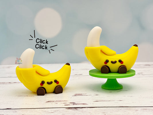 Two banana-shaped fidget clickers with faces on a wooden surface, one on a small green stand.