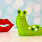Kawaii amigurumi ragdoll style crochet pattern for a Green crocheted slug toy next to a pair of red lips on a light blue background with white circles.