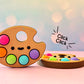 Colorful paint palette with kawaii face fidget clicker and 'Click Click' text on a blurred background
