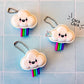 Three cloud-shaped fidget clicker keychains with rainbow tails on a tiled background