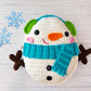Kawaii amigurumi ragdoll style crochet pattern for snowman plush toy with a blue scarf on a light wooden background
