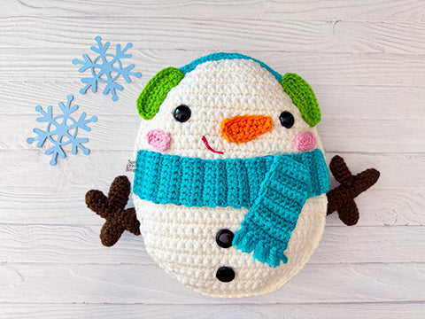 Kawaii amigurumi ragdoll style crochet pattern for snowman plush toy with a blue scarf on a light wooden background