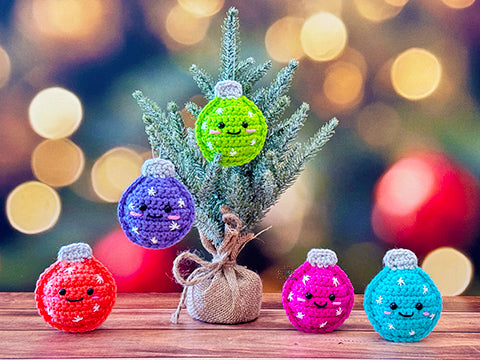 Kawaii amigurumi ragdoll style crochet pattern for a crocheted Christmas ornaments with faces on a wooden surface with a blurred festive background.