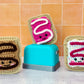 Small crocheted pop tarts on a cement surface with orange tile background