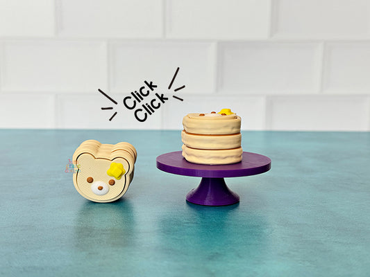 Bear-shaped pancake fidget clicker on a purple stand against a tiled wall background.