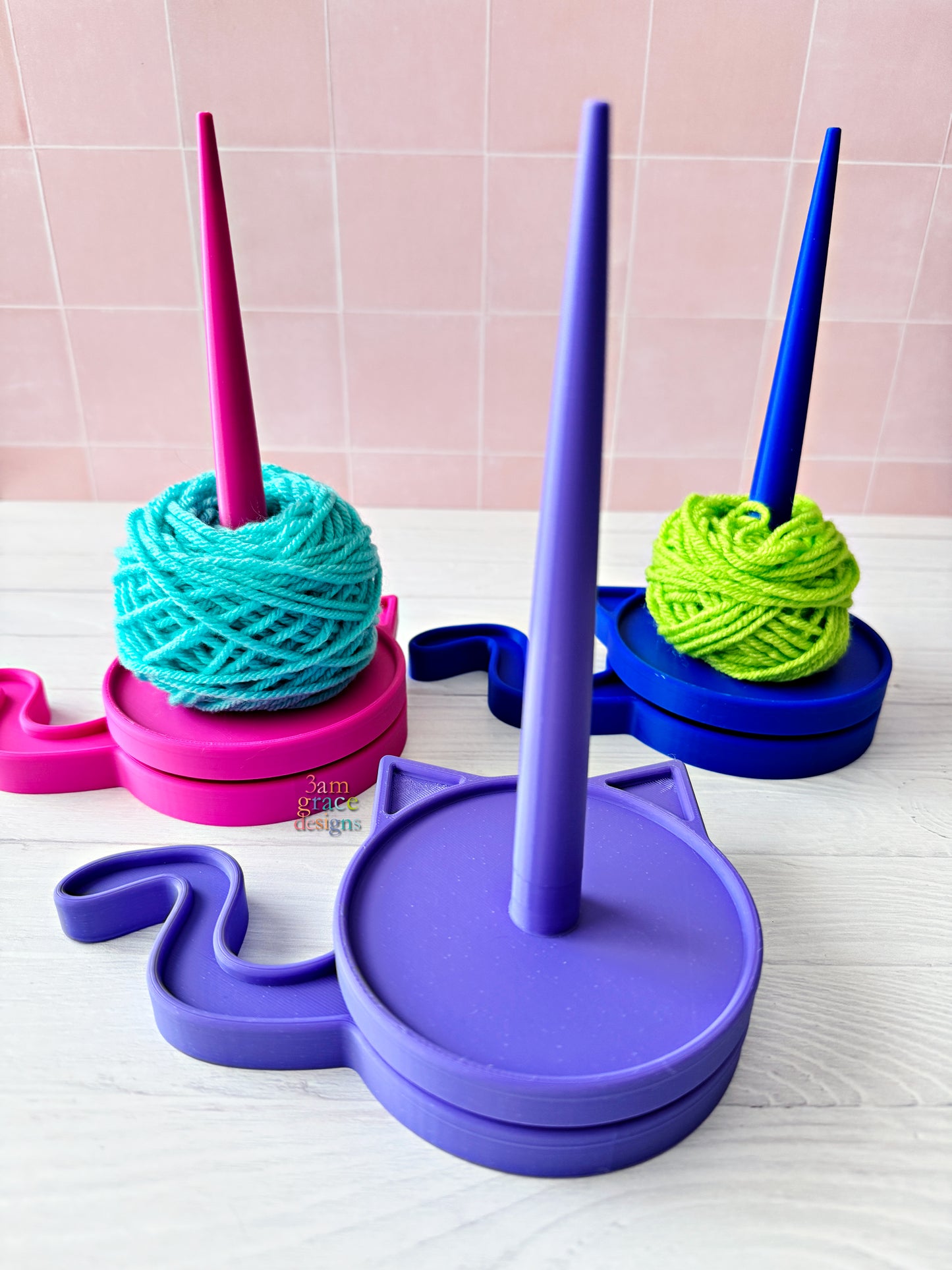 Colorful yarn spinner 3d printed yarn spinner tool in shape of cat in bright colors. Pictured on a light wooden surface with yarn on a tiled wall background