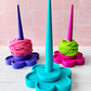 3d printed yarn spinner tool in shape of flower in bright colors. Pictured on a light wooden surface with a tiled wall background
