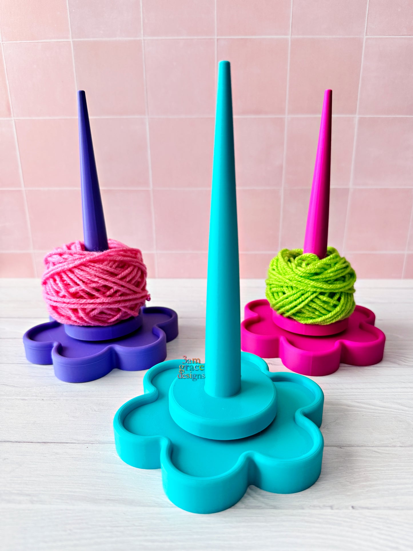 3d printed yarn spinner tool in shape of flower in bright colors. Pictured on a light wooden surface with a tiled wall background