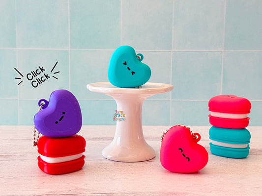 Heart macaron clicker keychain in purple, red, turquoise, and pink with a blue tile background