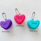 Three heart-shaped macaron keychains with different eye expressions on a light gray background.
