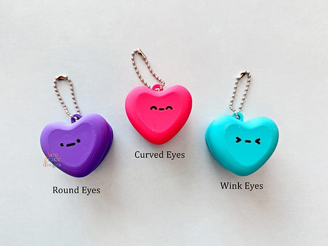 Three heart-shaped macaron keychains with different eye expressions on a light gray background.