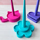 Colorful 3d printed yarn spinners on a light wooden surface with a pink tiled wall background.