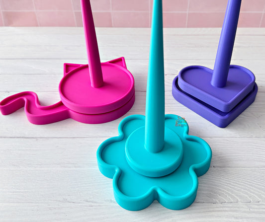 Colorful 3d printed yarn spinners on a light wooden surface with a pink tiled wall background.