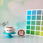 Latte coffee cup clickers on turquoise stand with colorful cube and bokeh background.