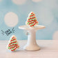 Two Christmas tree-shaped cookie fidget clicker on a white stand with a light blue background
