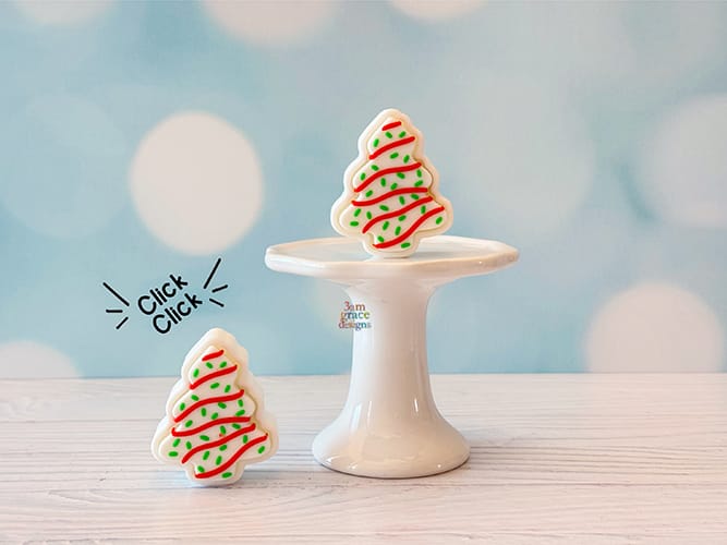 Two Christmas tree-shaped cookie fidget clicker on a white stand with a light blue background