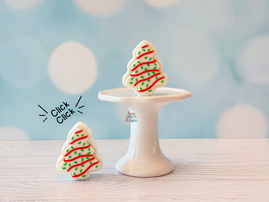 Two Christmas tree-shaped cookie fidget clicker on a white stand with a light blue background