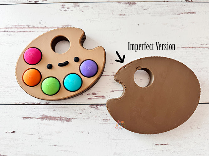 Colorful paint palette with kawaii face fidget clicker labeled 'Imperfect Version'.