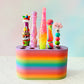 rainbow colored crochet hook stand with colorful crochet hooks on a blue background